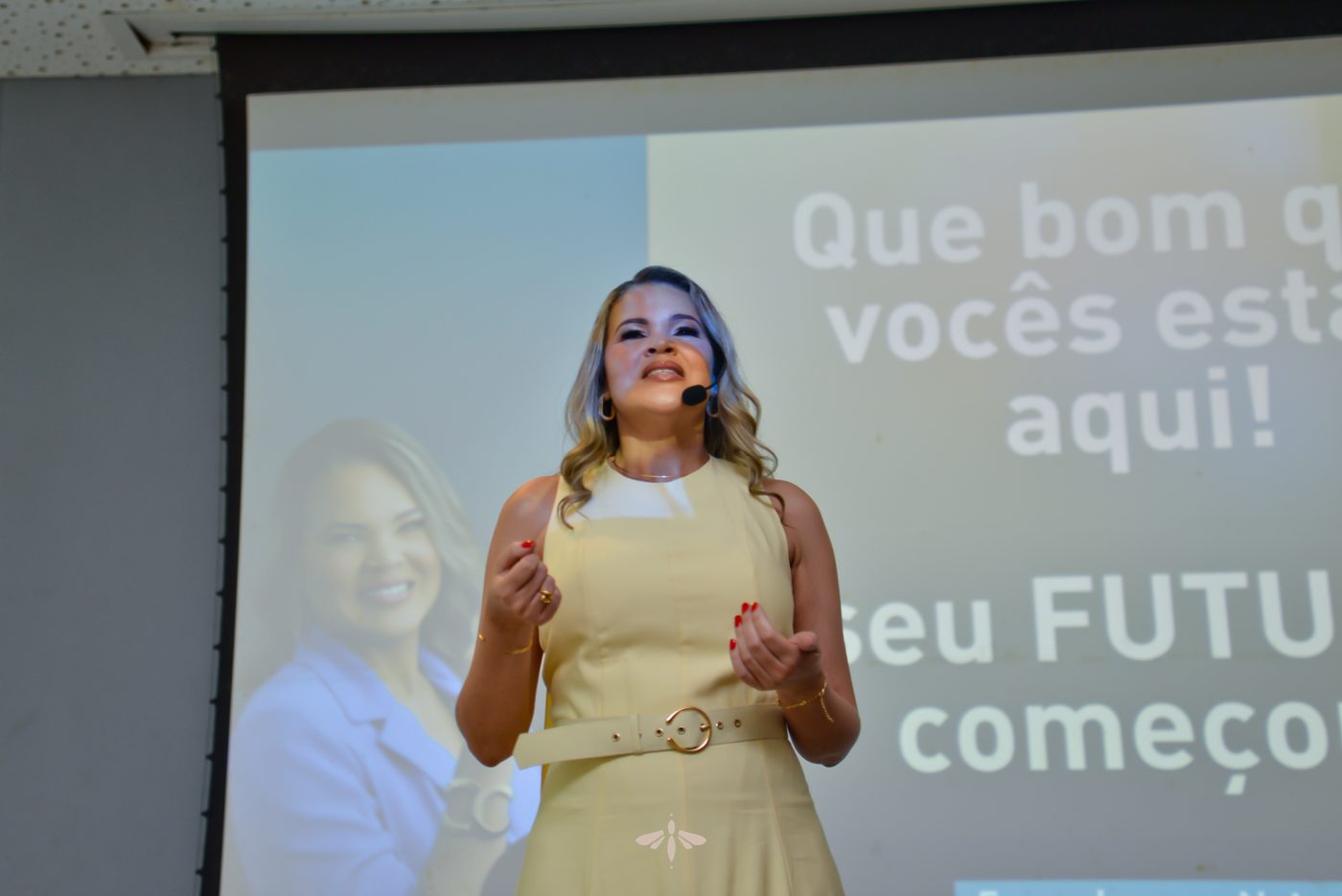 Palestrante no palco diante do telão com a frase Que bom que vocês estão aqui